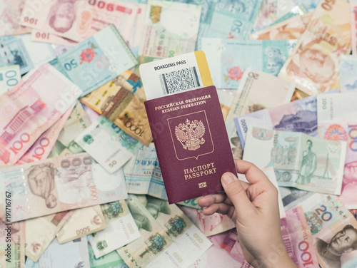 Female hand holding russian passport with boarding pass on Asia money background . Currency of Hong Kong, Indonesia, Malaysia, China, Thai, Singapore dollar. Travel and business concept 