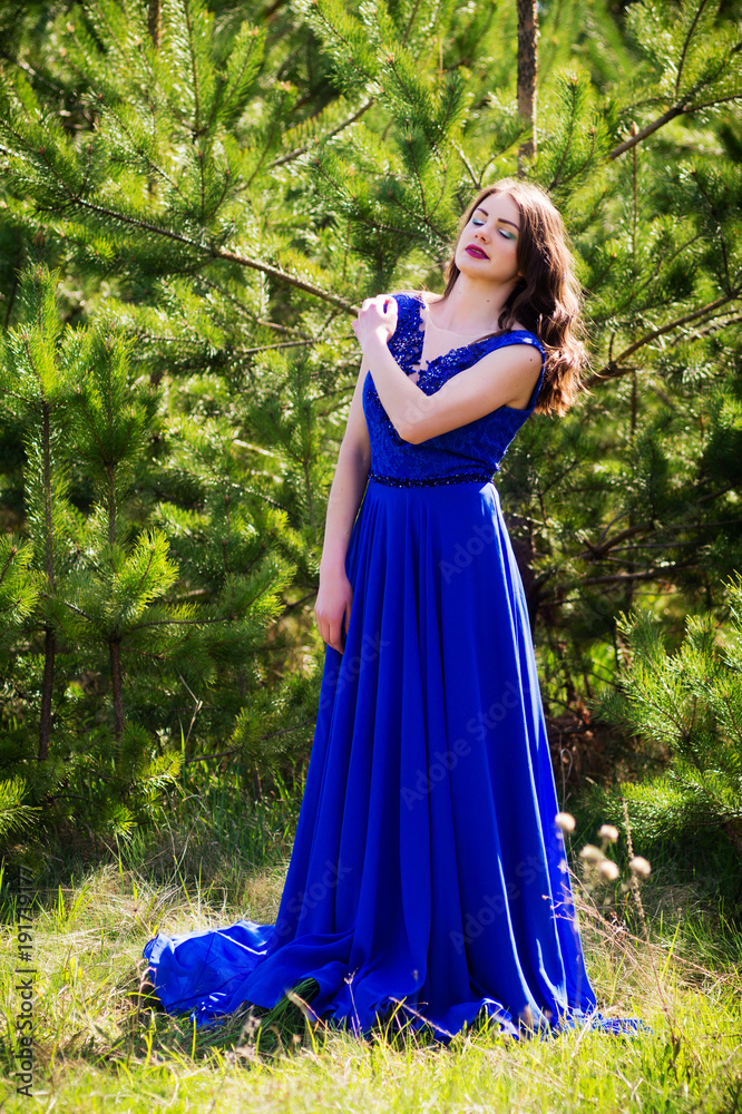Beautiful fashion model in a dress in a green park in the summer . Blue dress.