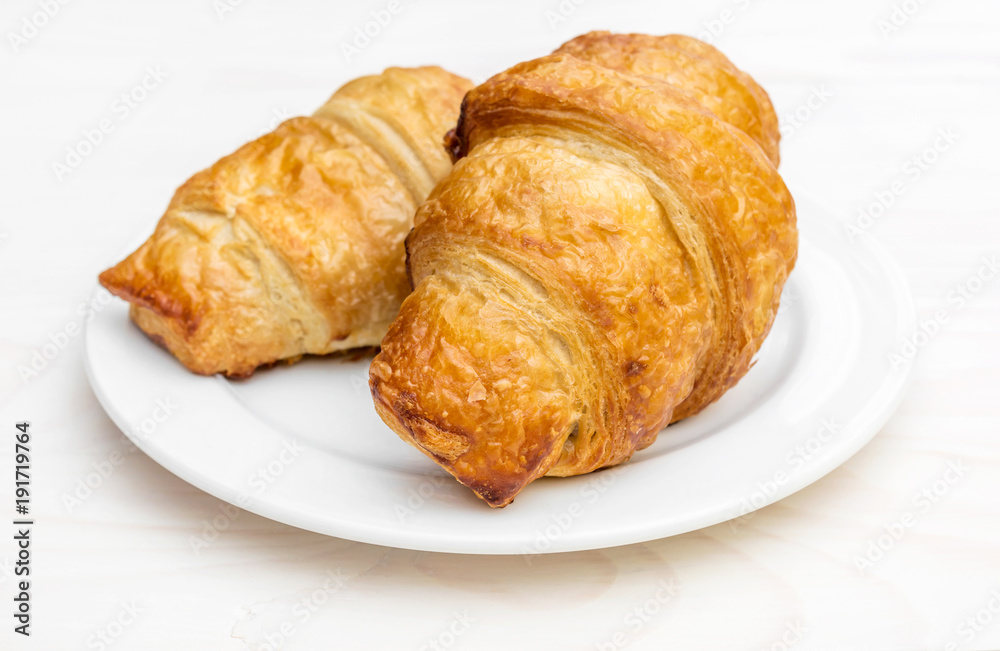 Plate with two croissants on the white wooden table. Close up.