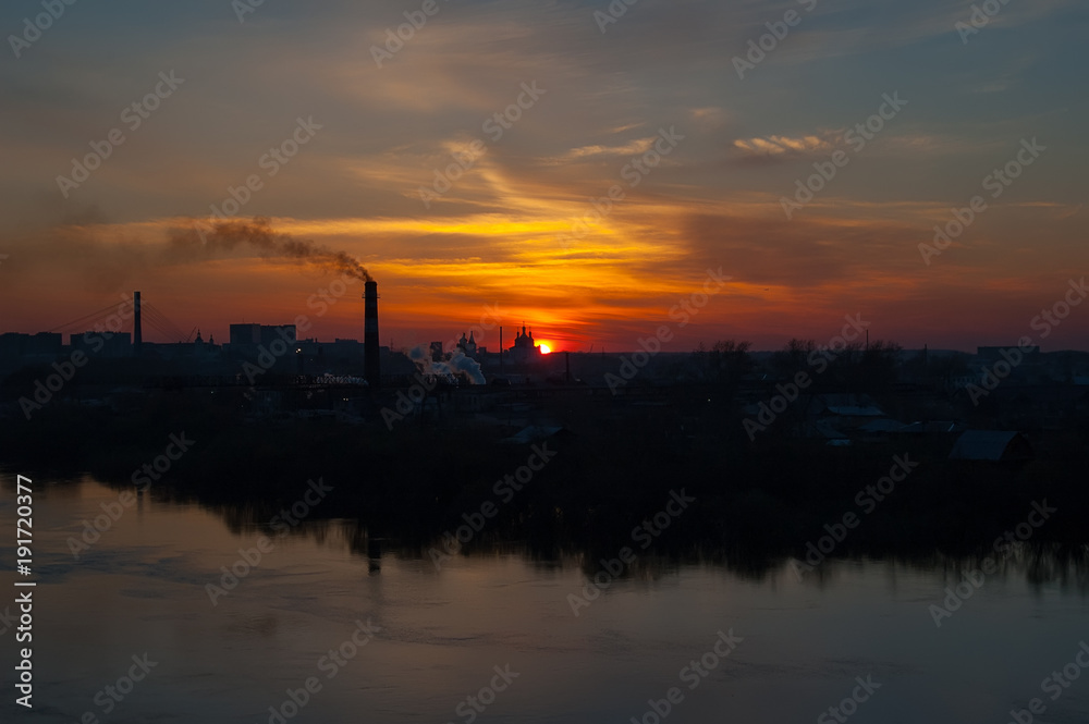 Tyumen, Russia - May 1, 2005: Silhouettes of plywood factory on river bank and Holy Trinity Monastery