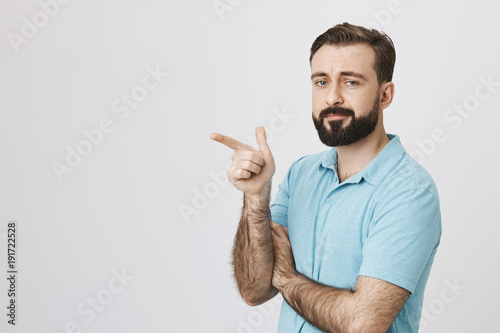 Person with a handsome beard and moustache wearing casual clothing pointing somewhere isolated on a white background. Tired consultant at store shows customer where is dressing room
