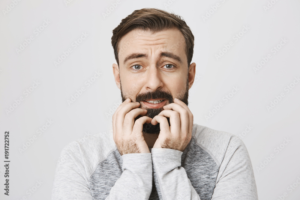 Close-up portrait of european man who expresses fear, holding hands on beard and looking afraid at camera, standing over gray background. Poor guy sail on boat and sees shark around him Close-up portrait of european man who expresses fear, holding hands on beard and looking afraid at camera, standing over gray background. Poor guy sail on boat and sees shark around him