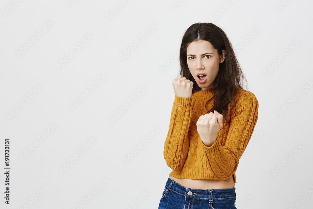 Portrait of confident european female model standing in boxer pose with raised fists as if wanting to attack someone, saying come on over gray background. Girl attended self-defence course Portrait of confident european female model standing in boxer pose with raised fists as if wanting to attack someone, saying come on over gray background. Girl attended self-defence course