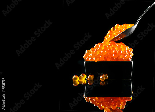 Caviar in a spoon. Salmon caviar in a bowl over black background. Closeup trout caviar