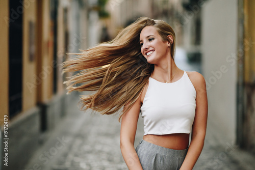 Happy young woman with moving hair in urban background.