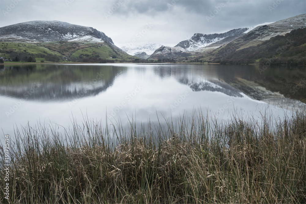 Beautiful Winter landscape image of Llyn Nantlle in Snowdonia National Park with snow capped mountains in background
