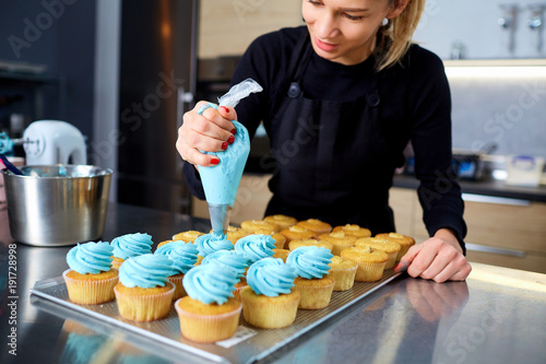 Photography The confectioner with a pipping bag of cream in his hands decoretion cupcake on the table in the kitchen of a pastry shop