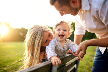 Happy family in a park in summer autumn. Mother, father and baby play in nature in the rays of sunset.