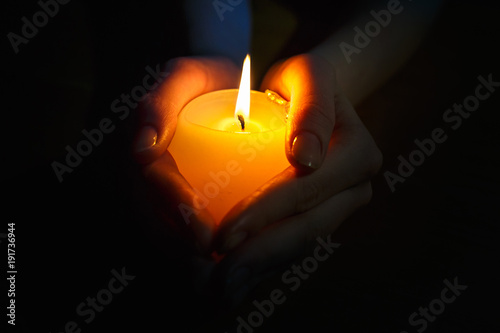 burning candle in the hands of a praying girl on a black background