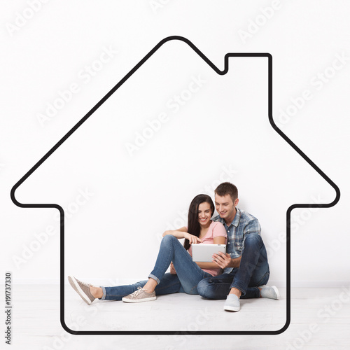 Fotografie Happy young couple sitting on floor using a tablet for shopping and entertainment