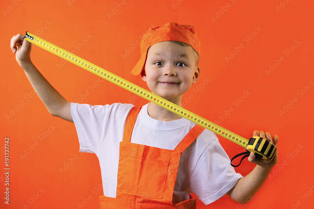 funny builder boy holding a tape measure on an orange background funny builder boy holding a tape measure on an orange background