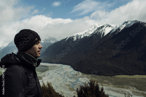 Hombre joven con gorro de perfil observando montañas con picos nevados en Nueva Zelanda