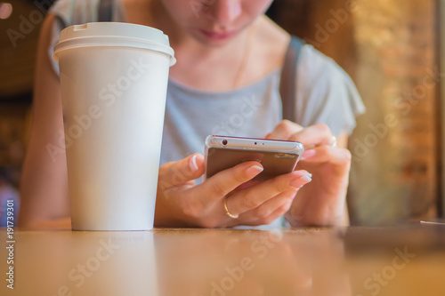 Fototapeta Naklejka Na Ścianę i Meble -  A girl is sitting with a phone in a cafe, a coffee house