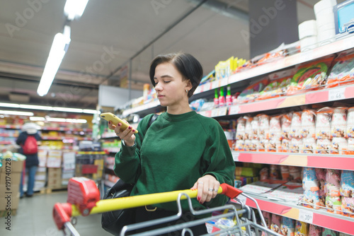 Portrait of a girl using a phone in a supermarket. A beautiful girl with a short haircut looks at the shopping list at the supermarket.