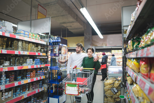 A young couple rides a supermarket with a shopping carts and buys products. Family shopping at a supermarket