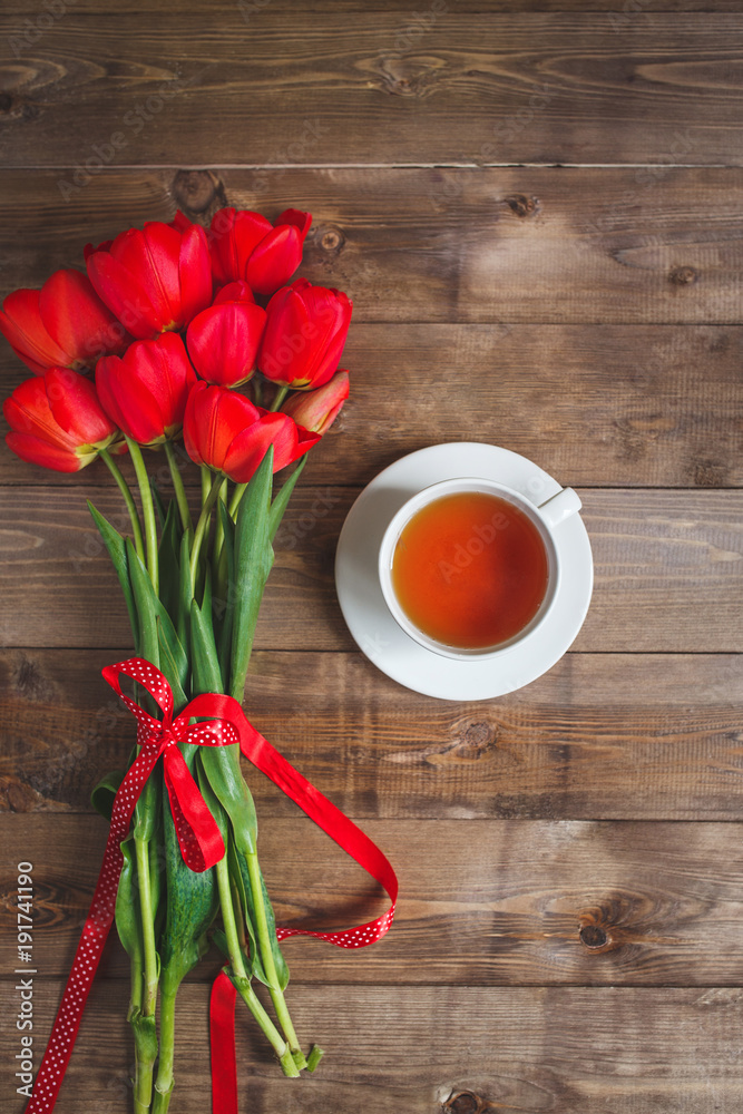 A cup of tea red tulips pattern on wooden background . Valentines Day and Mother's Day background . A cup of tea red tulips pattern on wooden background . Valentines Day and Mother's Day background .