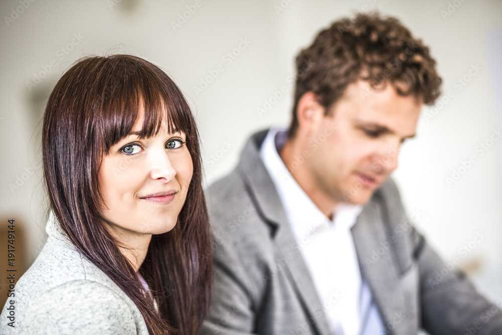 Portrait of beautiful young businesswoman with male colleague in background at office Portrait of beautiful young businesswoman with male colleague in background at office