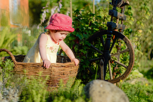 A cute little girl sits on a hay in a basket in the garden