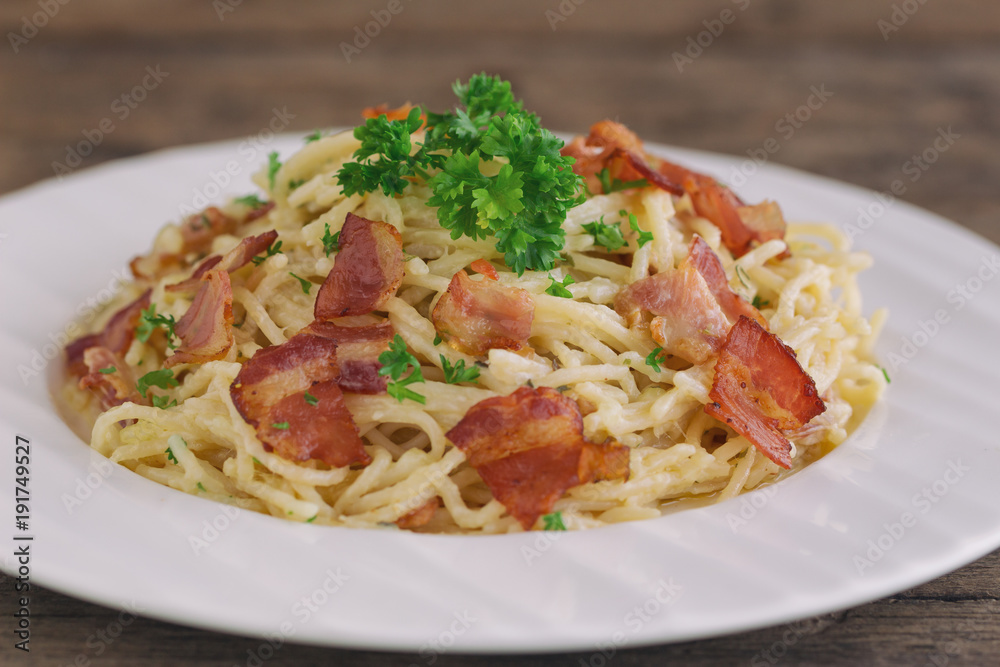 Spaghetti carbonara with bacon and cheese on white plate sprinkle with chopped parsley on wood table in close up view. Italian traditional homemade food for lunch or dinner so creamy and delicious.