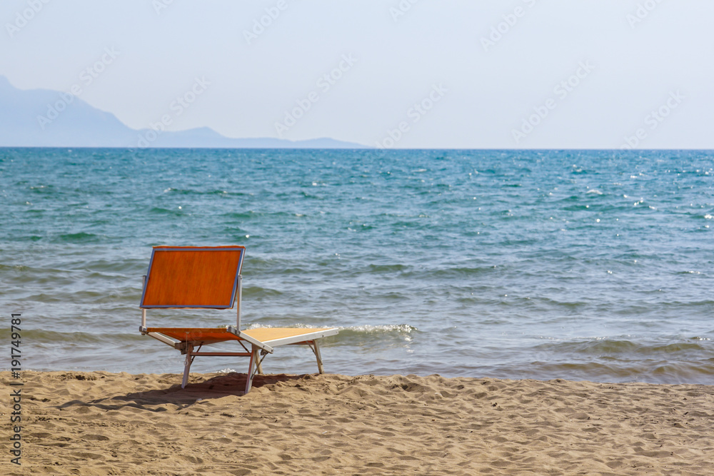 Bright chaise lounge on sand on seashore. Against background of sea