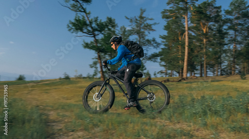 Fat bike also called fatbike or fat-tire bike in summer riding in the forest. The guy rides a bicycle among trees and stumps. He overcomes some obstacles on a bumpy road.