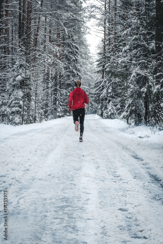 Athletic fit Caucasian female jogging in winter forest, trees covered with snow