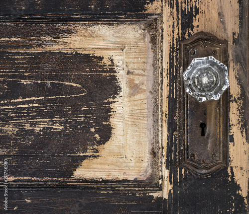 Old weathered antique beat-up wood panel door with chipped peeling paint and glass crystal doorknob and rusted plate