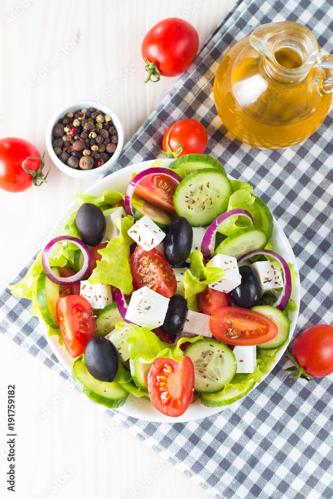 Fresh Greek salad made of cherry tomato, ruccola, arugula, feta, olives, cucumbers, onion and spices. Caesar salad in a white bowl on wooden background. Healthy organic diet food concept. Fresh Greek salad made of cherry tomato, ruccola, arugula, feta, olives, cucumbers, onion and spices. Caesar salad in a white bowl on wooden background. Healthy organic diet food concept.