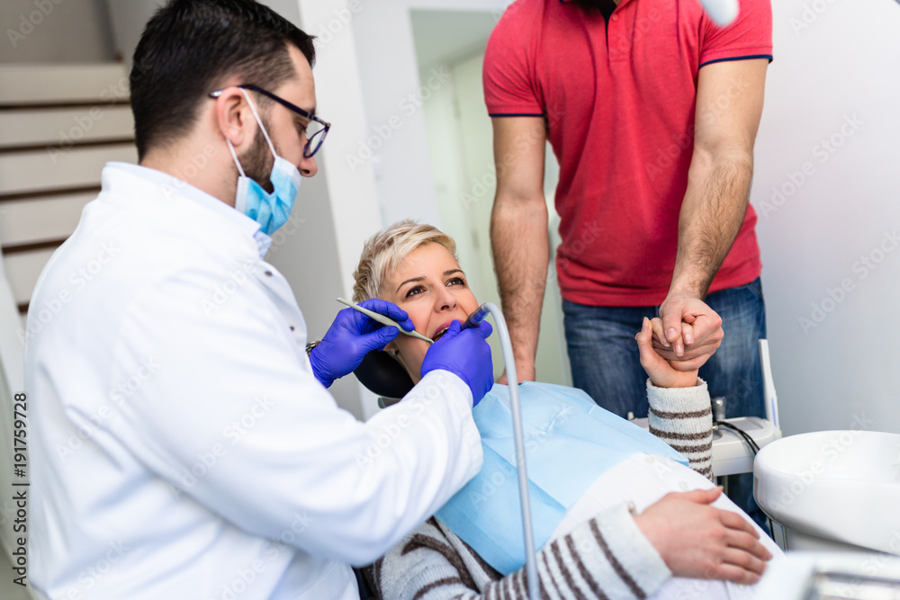 Obraz premium Attractive bearded man with his pregnant wife having medical treatment in dental office