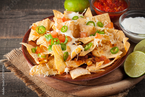 Corn Mexican nachos with beef, jalapeno, cheese, pepper, olives and chili con carne on a wooden background. Lime, Ketchup, sour cream and mayonnaise souce seasoning. photo