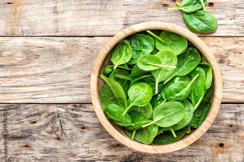 Fresh baby spinach leaves in bowl on wooden background