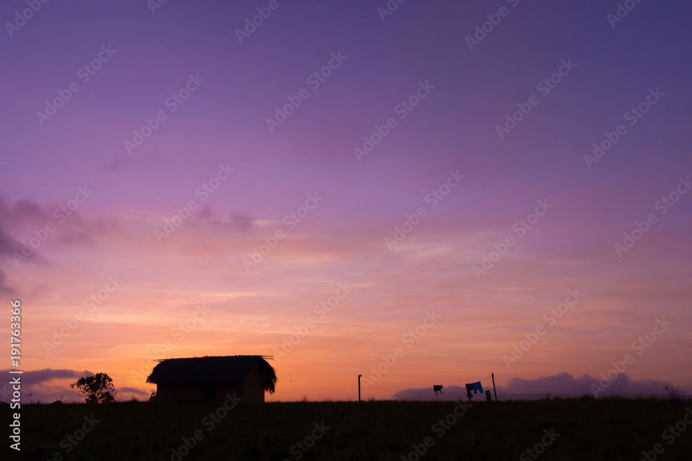 The silhouette of the hut with drying laundry on sunset sky background
