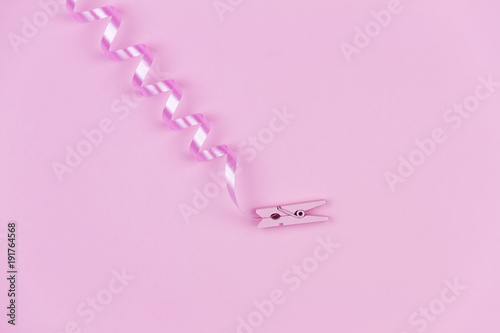 Pink clothespin lying on center with pink curved tape on pink background.