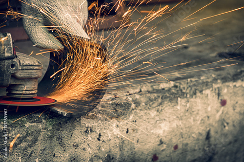 Worker using  grinder in workshop and throwing sparks.
