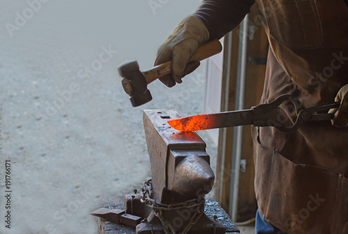 The blacksmith precisely hammers out a piece of red hot metal in order to construct a fixed blade knife.