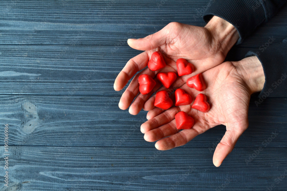Male hands with red candies in a form of heart on the dark blue wooden background.