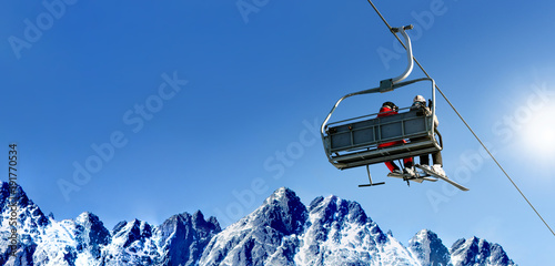 Composite image of skiers on a ski lift in high mountains on the background of a clear blue sky with large copy space. photo