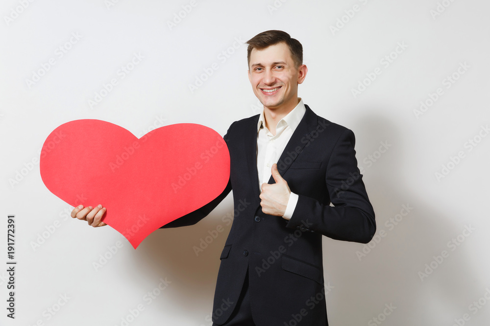 Young man in suit showing thumb up holding big red heart isolated on white background. Copy space, advertisement. Place for text. St. Valentine's Day, International Women Day birthday holiday concept. Young man in suit showing thumb up holding big red heart isolated on white background. Copy space, advertisement. Place for text. St. Valentine's Day, International Women Day birthday holiday concept.