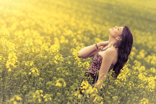 Beautiful woman in meadow of yellow flowers with head up. Attractive genuine young girl enjoying the warm summer sun in wide green yellow meadow. Experimental inclined plane. Part of series © azur13