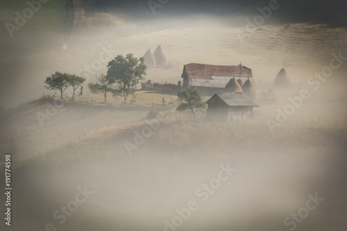 Beautiful rural mountain landscape in the morning light with fog, old houses and haystacks, Fundatura Ponorului, Hunedoara County, Romania photo