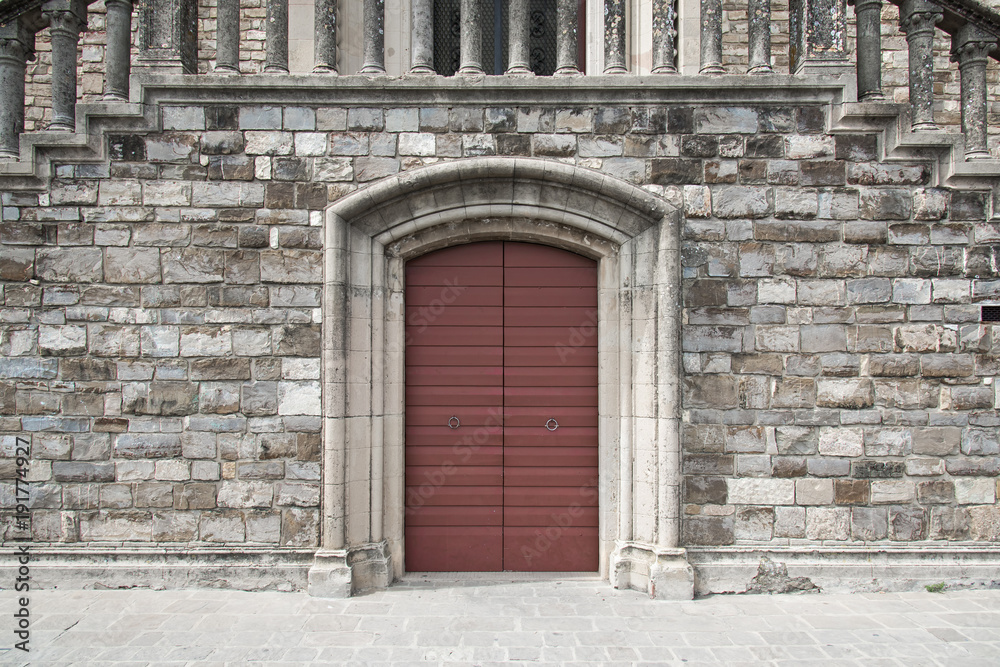 Burgundy door in stone wall with elaborate frame Burgundy door in stone wall with elaborate frame