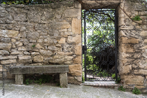 Fototapeta Naklejka Na Ścianę i Meble -  Iron gate in ancient stone wall with bench