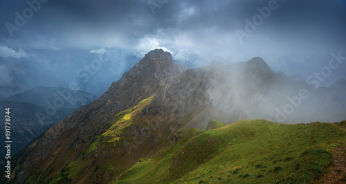 Mountain tops under low thunderclouds and rain. Highlighted green grassy valleys