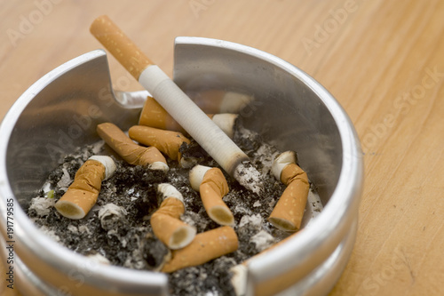 Ashtray full of extinguished cigarette butts with one lit