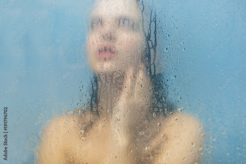 Woman bathes in shower cabine, poses naked against blurred sweat glass background with drops, feels relaxation and freshness, dreams about something pleasant. Body care and lifestyle concept