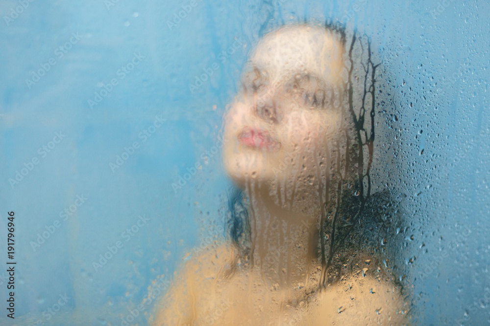 Nude female with wet hair poses in shower booth against blurred sweat
