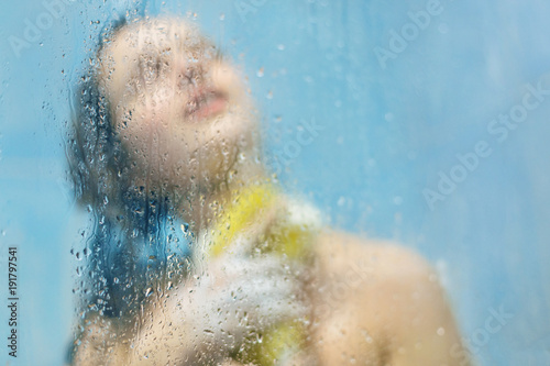Portrait of relaxed slender woman poses with naked body at shower cabine, has wet perfect body, silhouette against sweat blurred background with water drops. Health and body care concept