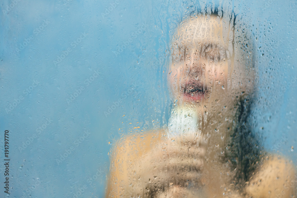 Relaxed carefree woman washes herself in douche, sings loudly, pretends to  be successful talented singer, enjoys loneliness at home, poses behind  blurred glass with water drops and copy space for text Stock