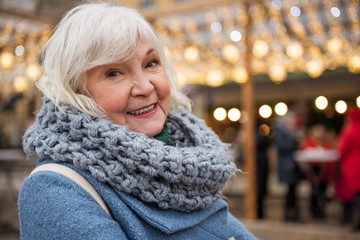 Portrait of excited senior woman enjoying winter holidays on street. She is looking at camera and smiling. Copy space