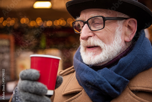 Portrait of cheerful mature man enjoying hot beverage while standing outside